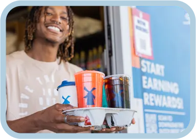 Person holding a tray with colorful Dutch Bros coffee cups outside a store with "START EARNING REWARDS" sign.