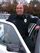 A uniformed police officer is shown smiling outside his cruiser