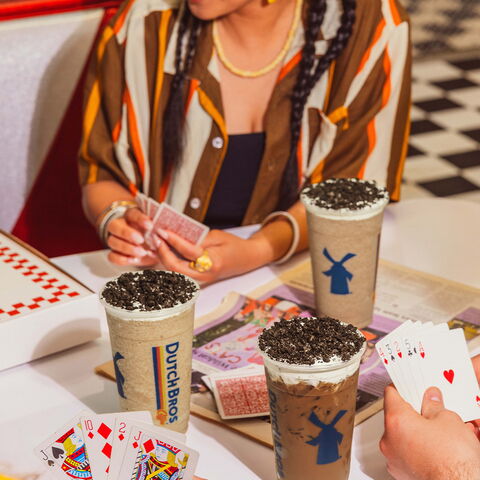 A group plays cards at a table with a trio of Dutch Bros drinks